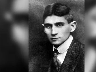 en:A black and white portrait of a young man with short, dark hair, wearing a tweed jacket and tie. ;fr:Un portrait en noir et blanc d'un jeune homme aux cheveux sombres coupés court,  vêtu d'une veste en tweed et d'une cravate.