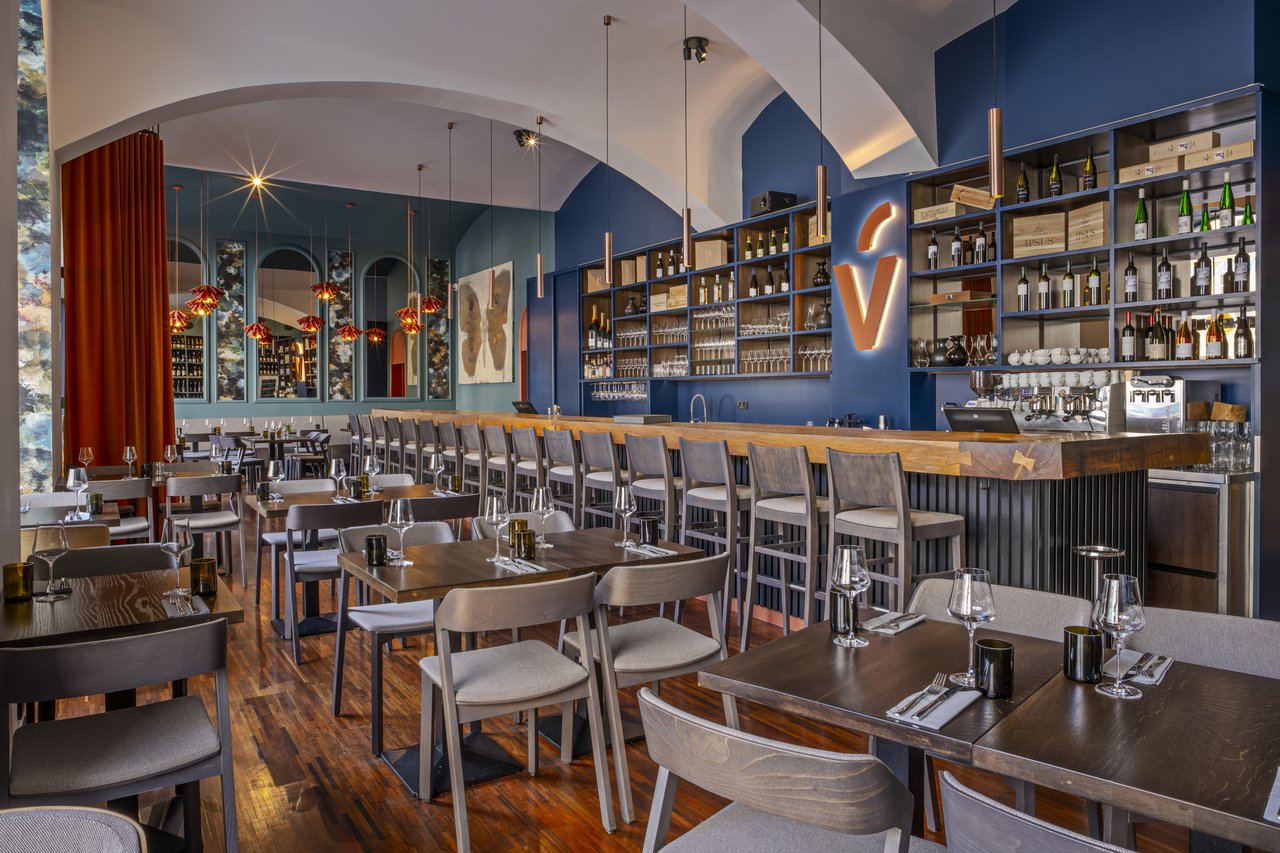 Large dining room with tables and a bar in the background featuring several bottles