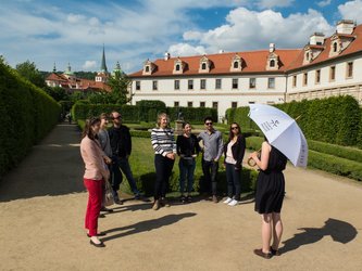 en:A tour guide, holding an umbrella, is speaking to seven people in a beautiful garden ;fr:Un guide touristique, un parapluie à la main, s'adresse à sept personnes dans un magnifique jardin