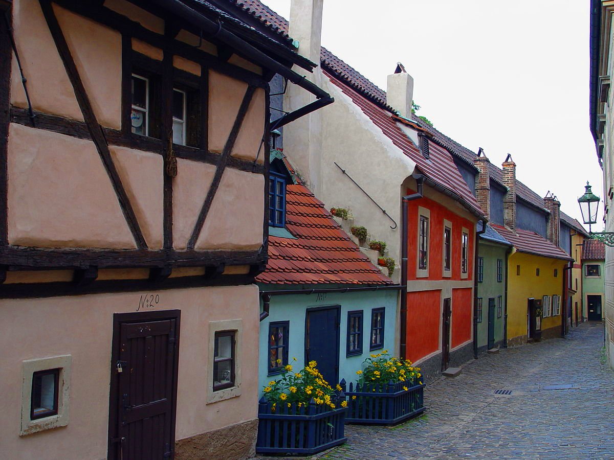 A narrow street in Prague lined with colorful houses featuring various architectural styles