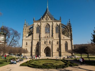 en:A large stone church with very pointed roofs rises behind a garden of green lawn and colorful flowers. ;fr:Une grande église en pierre aux toits très pointus s'élève derrière un jardin d'une pelouse verte et de fleurs coloré