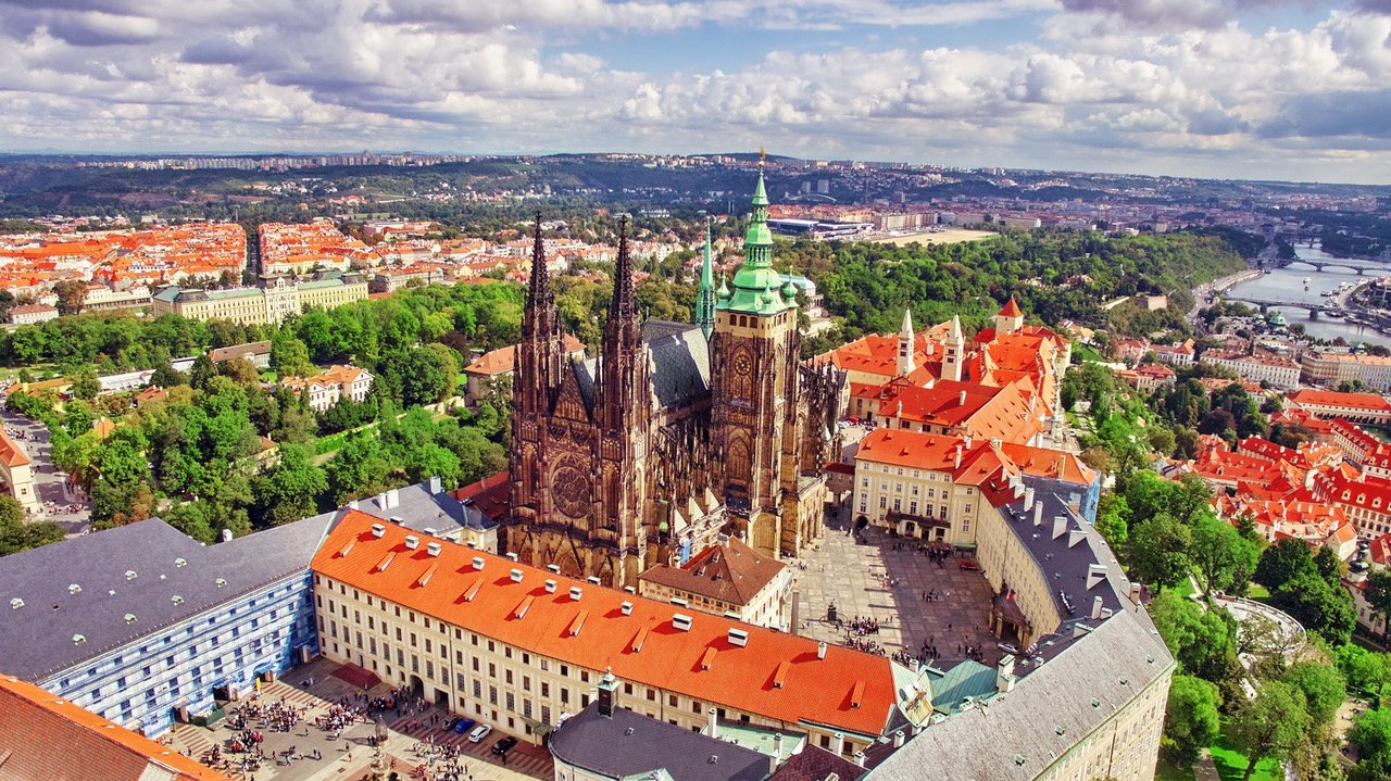 Aerial view of the Gothic cathedral at Prague Castle, surrounded by tall buildings with orange-colored roof tiles