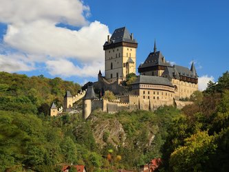 en:A beige Gothic fortress with five small towers and black roofs, situated on a hill ;fr:Une forteresse gothique beige, dotée de cinq petites tours et de toits noirs, située sur une colline