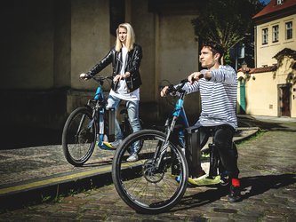 en:Two people on an electric scooter, gazing toward the horizon, riding along the cobblestone streets of Prague ;fr:Deux personnes sur une trottinette électrique, le nez rivé vers l'horizon, roulant sur les rues pavées de Prague