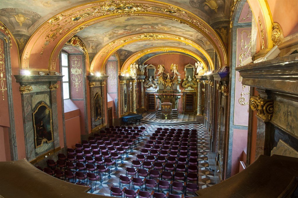 A long row of chairs in a chapel with colorful walls adorned with gold